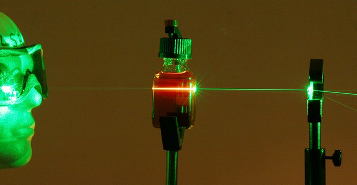 Laserstrahlung regt die Moleküle an, die ihrerseits die absorbierte Energie in Form von intensiver oranger Fluoreszenzstrahlung abgeben. Auch hinter dem Gefäß ist die Strahlung sehr intensiv und beleuchtet den Messkopf deutlich.