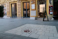 Diese Rose von Sarajewo und die weiße Gedenktafeln an der Mauer des Gebäudes dahinter erinnern an die Opfer eines Granateneinschlags während der Belagerung der Stadt. (Foto: RedTD/Keusch) 