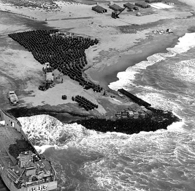 Flugzeugteile und befüllte Fässer warten auf den Abtransport. (Foto: US Naval Historical Center; gemeinfrei)