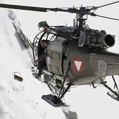 Das Foto zeigt das Werfen eines Lawinensprengsatzes aus einem Hubschrauber.