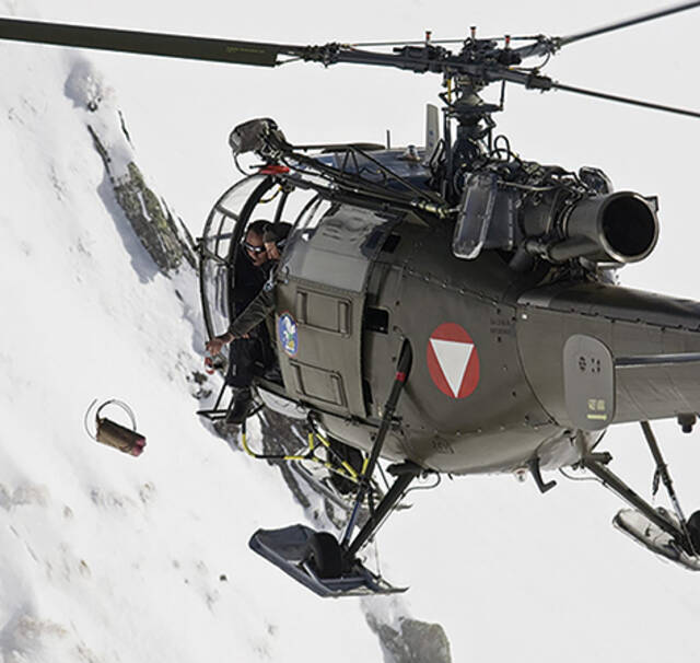 Das Foto zeigt das Werfen eines Lawinensprengsatzes aus einem Hubschrauber.